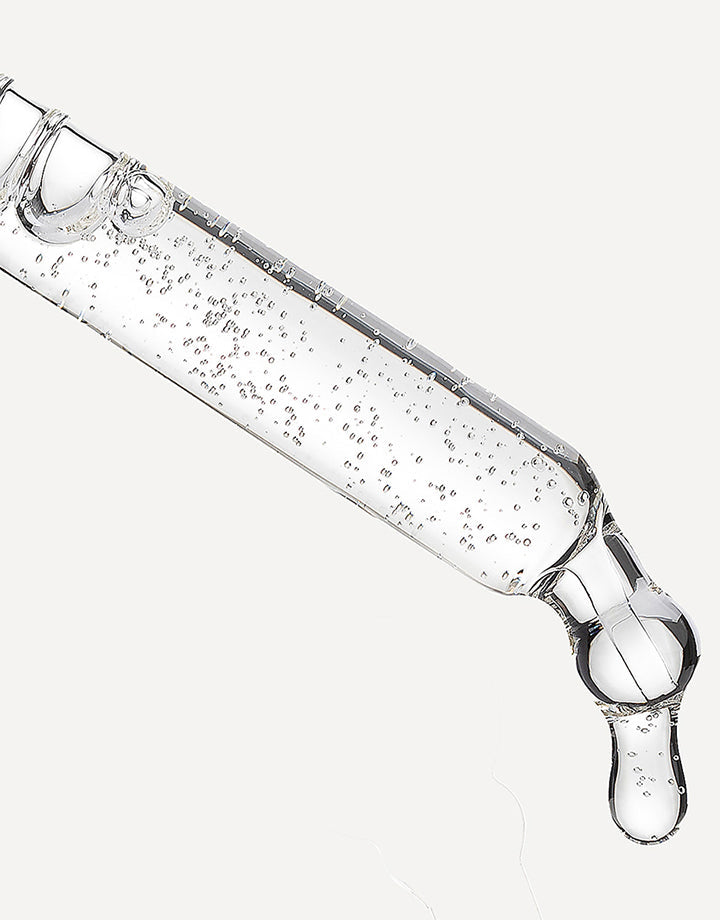 Pipeta con sérum transparente liberando una gota sobre fondo neutro.