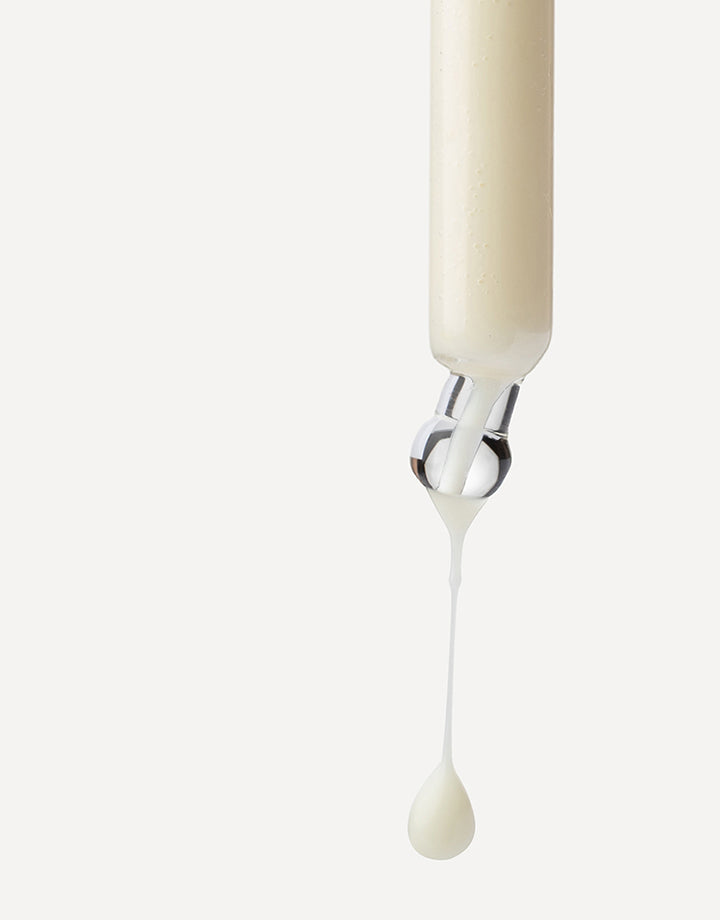 Pipeta con sérum denso crudo liberando una gota sobre fondo neutro.