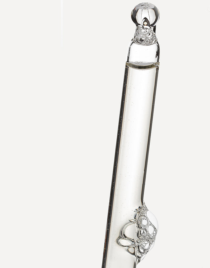 Pipeta con sérum transparente liberando una gota sobre fondo neutro.